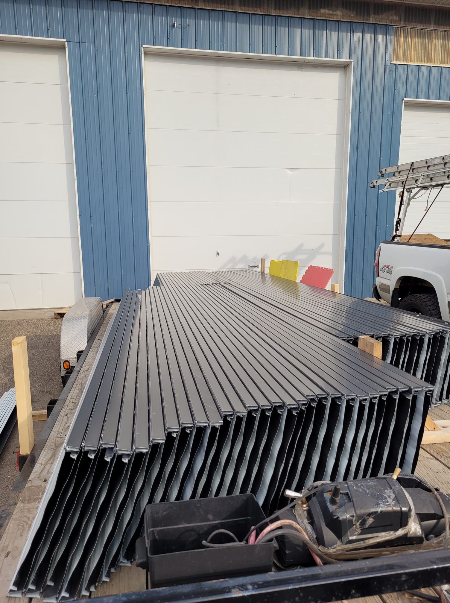 A truck is parked in front of a building with a bunch of metal pieces stacked on top of each other.