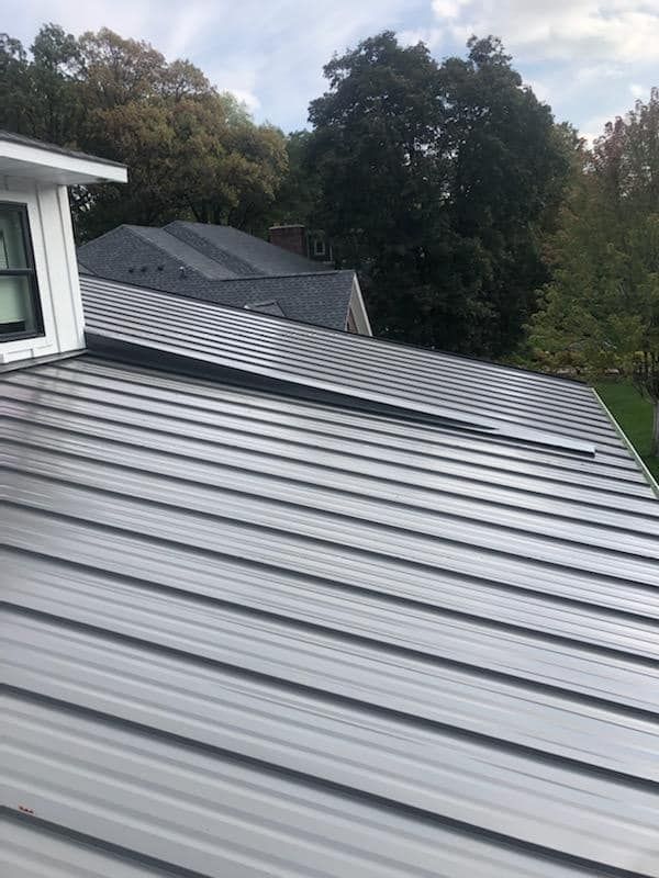 A close up of a metal roof on a house with trees in the background.