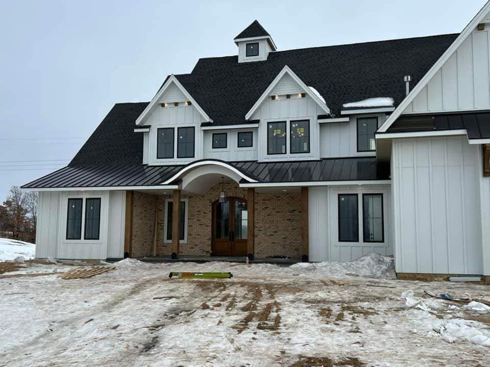 A large white house with a black roof is sitting in the snow.