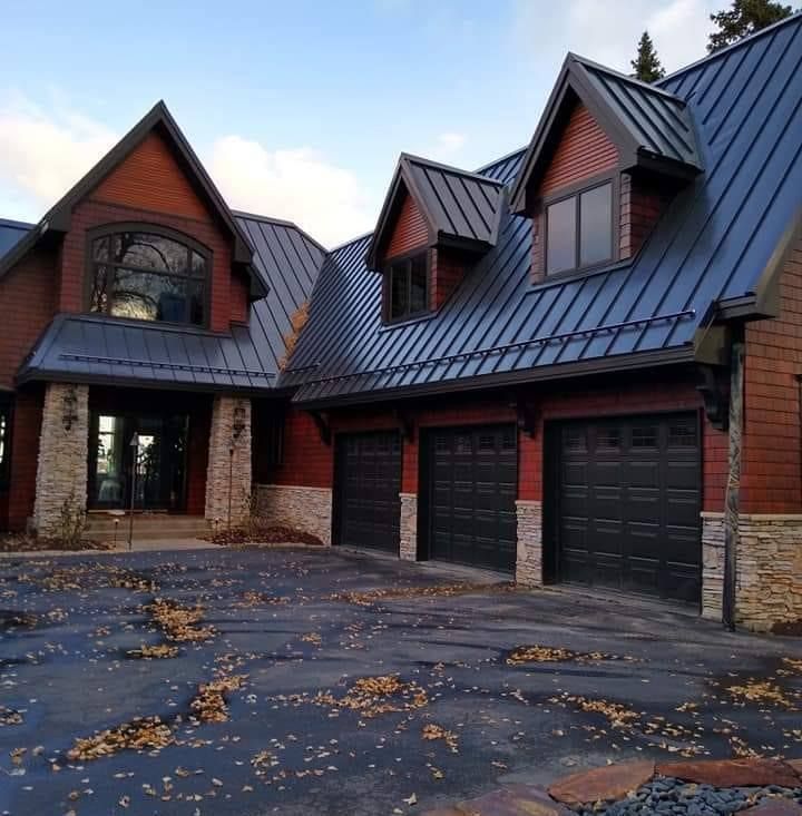 A large brick house with a blue roof and black garage doors