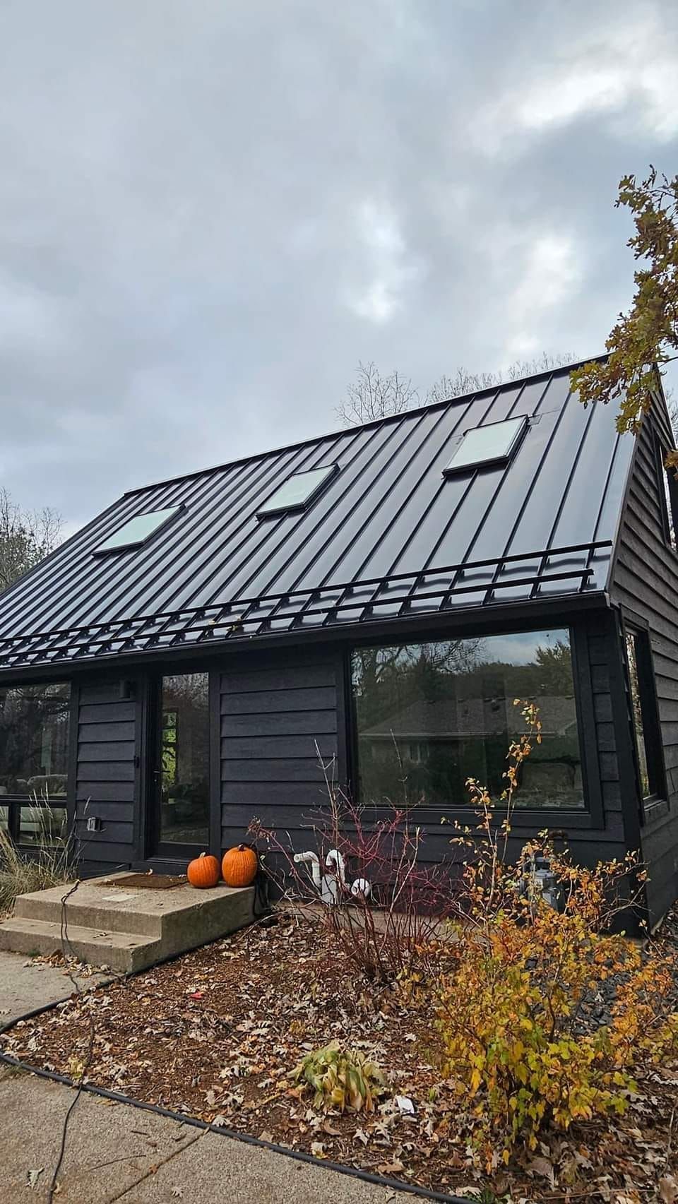 A black house with a black roof and two pumpkins in front of it.