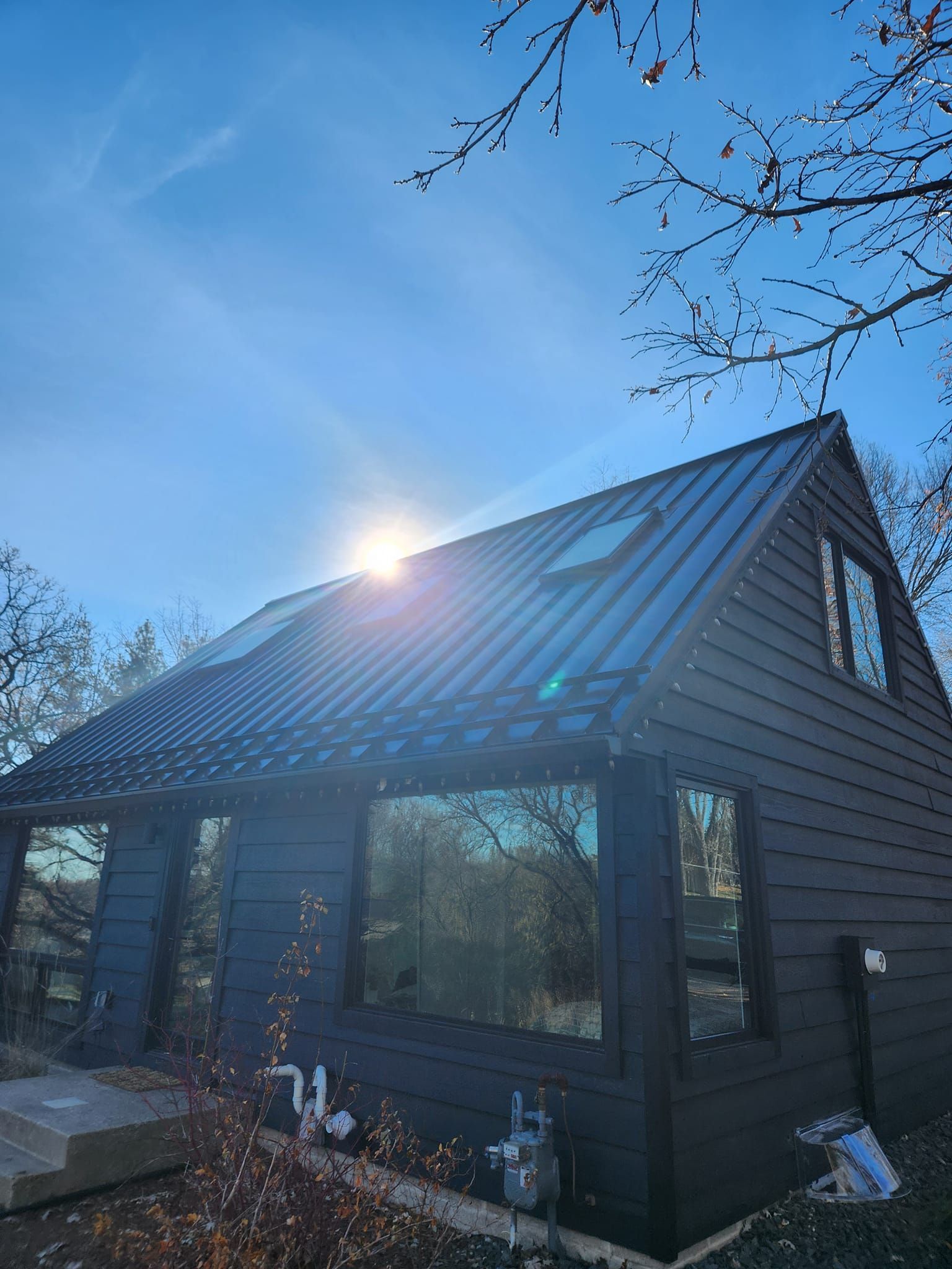 A black house with a metal roof and a blue sky in the background.