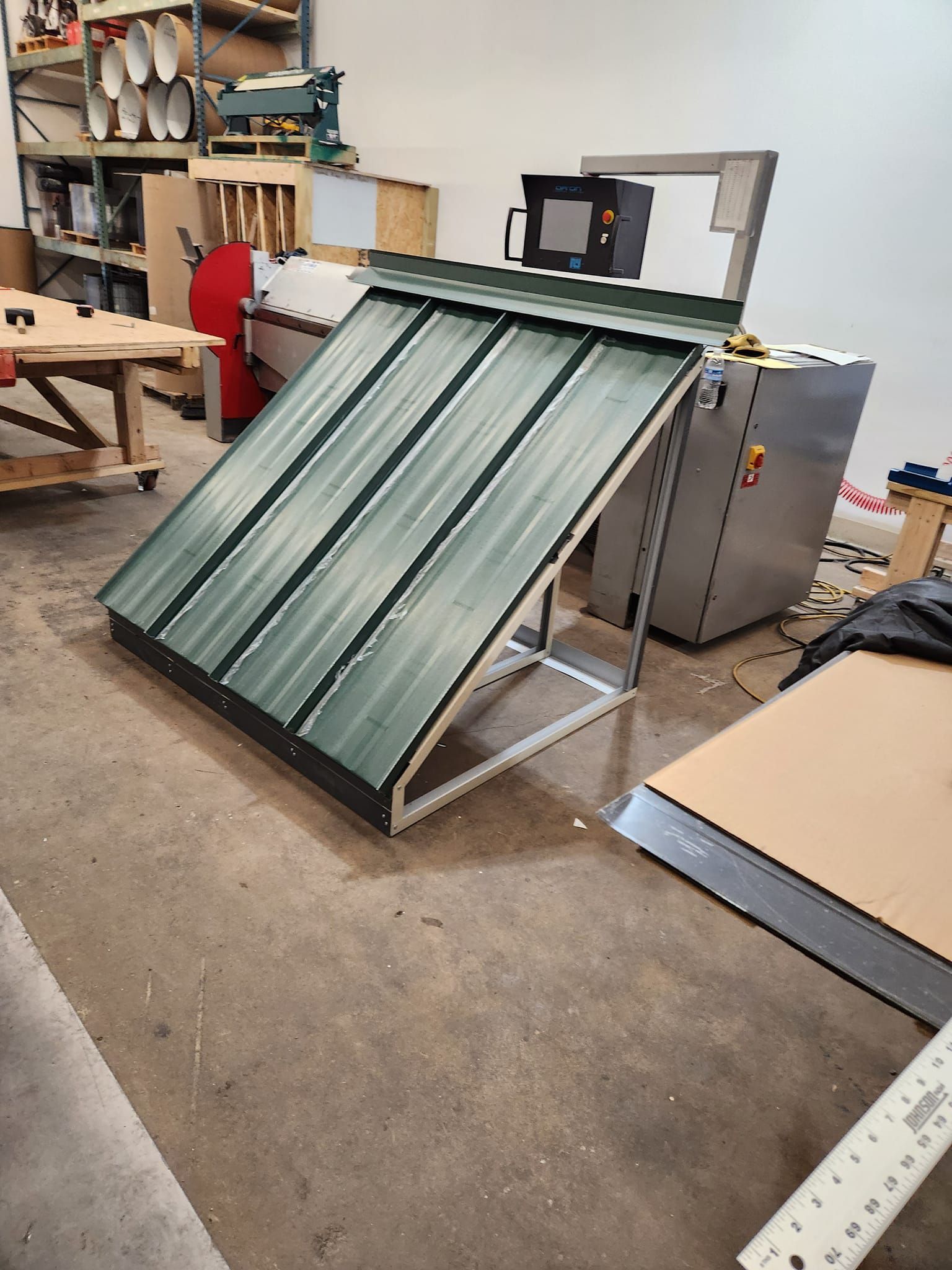 A green metal roof is sitting on the floor in a workshop.