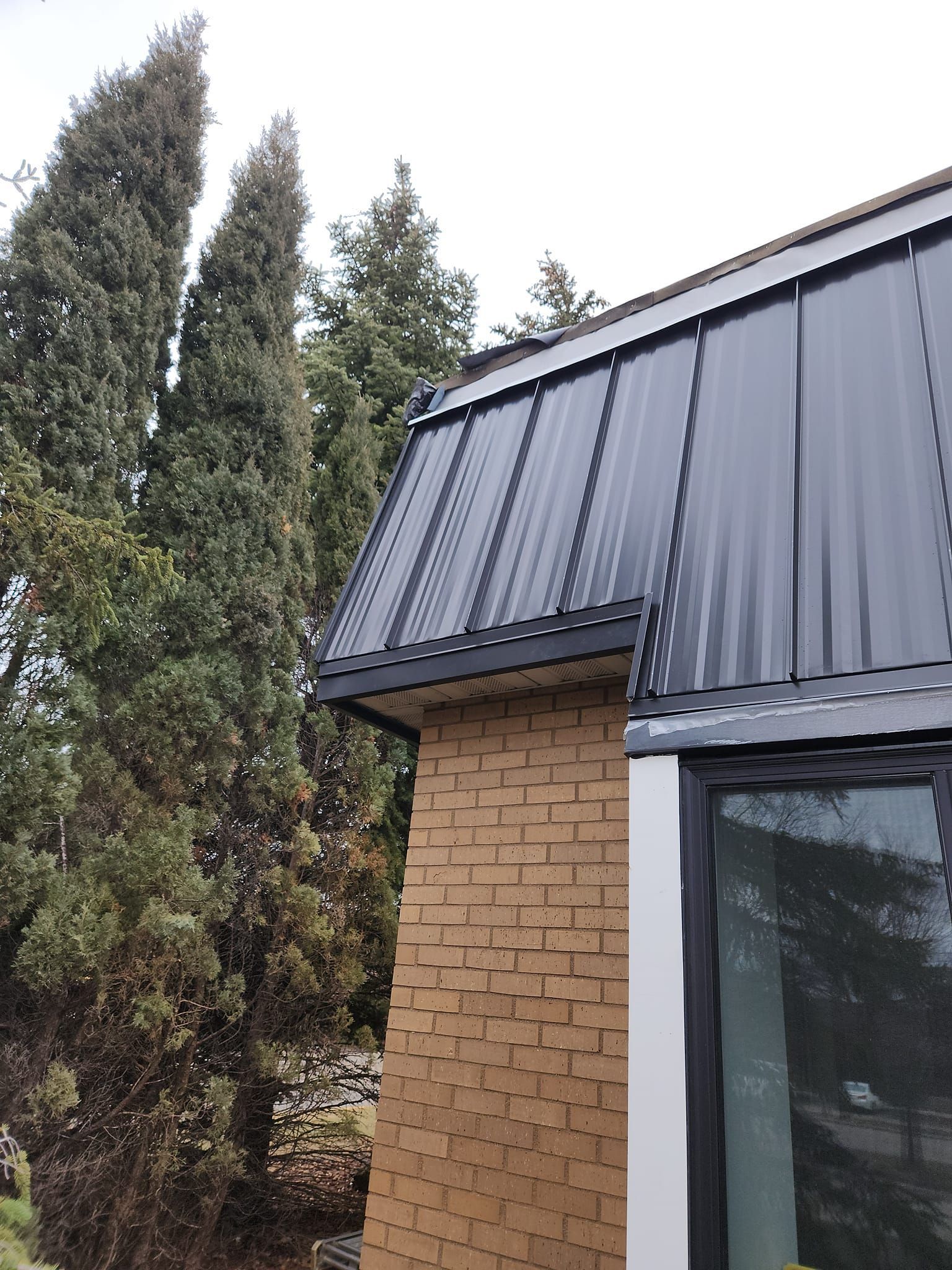 A brick building with a black roof and trees in the background.