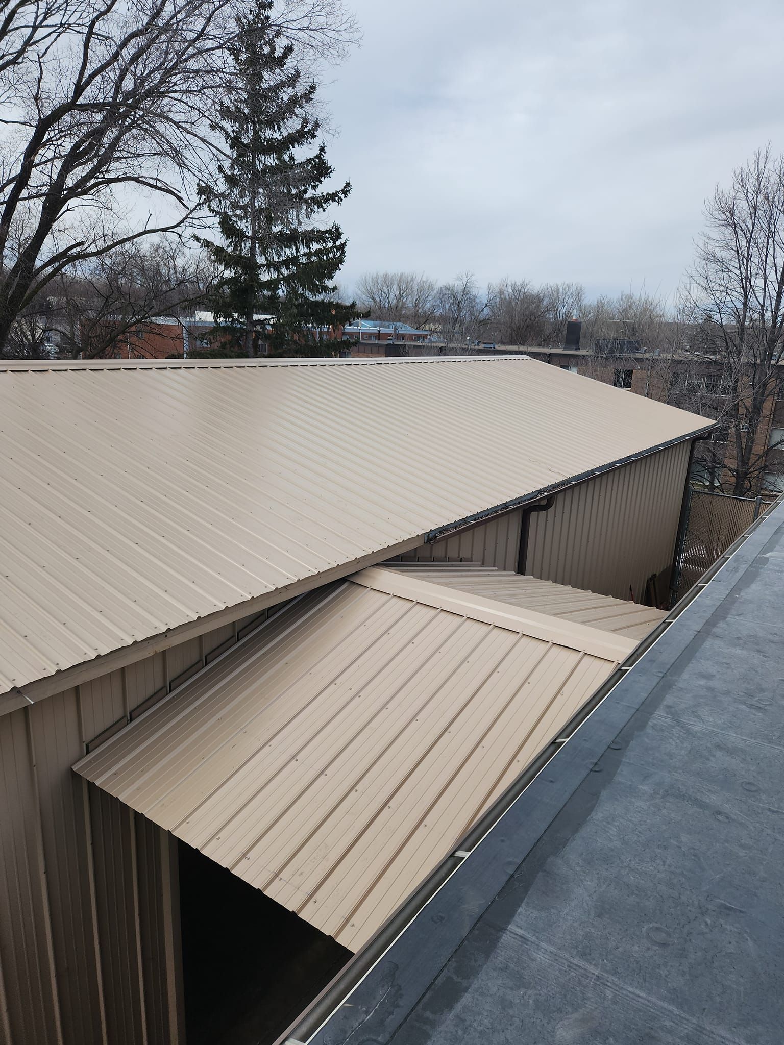 The roof of a building with a metal roof and trees in the background.