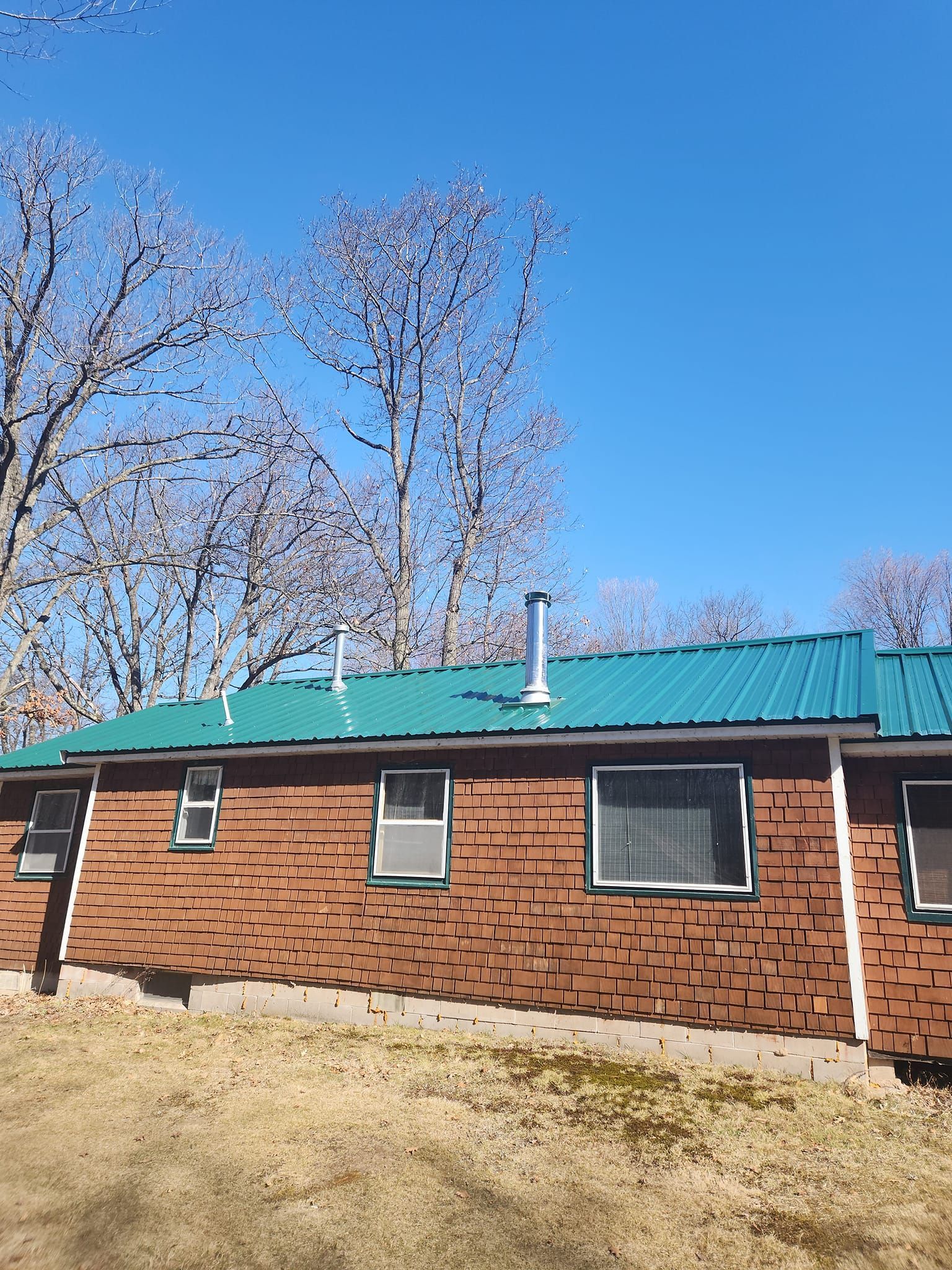 A brick house with a green roof and trees in the background.