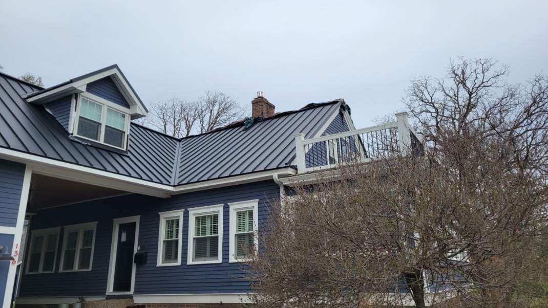 A blue house with a black metal roof and white windows.