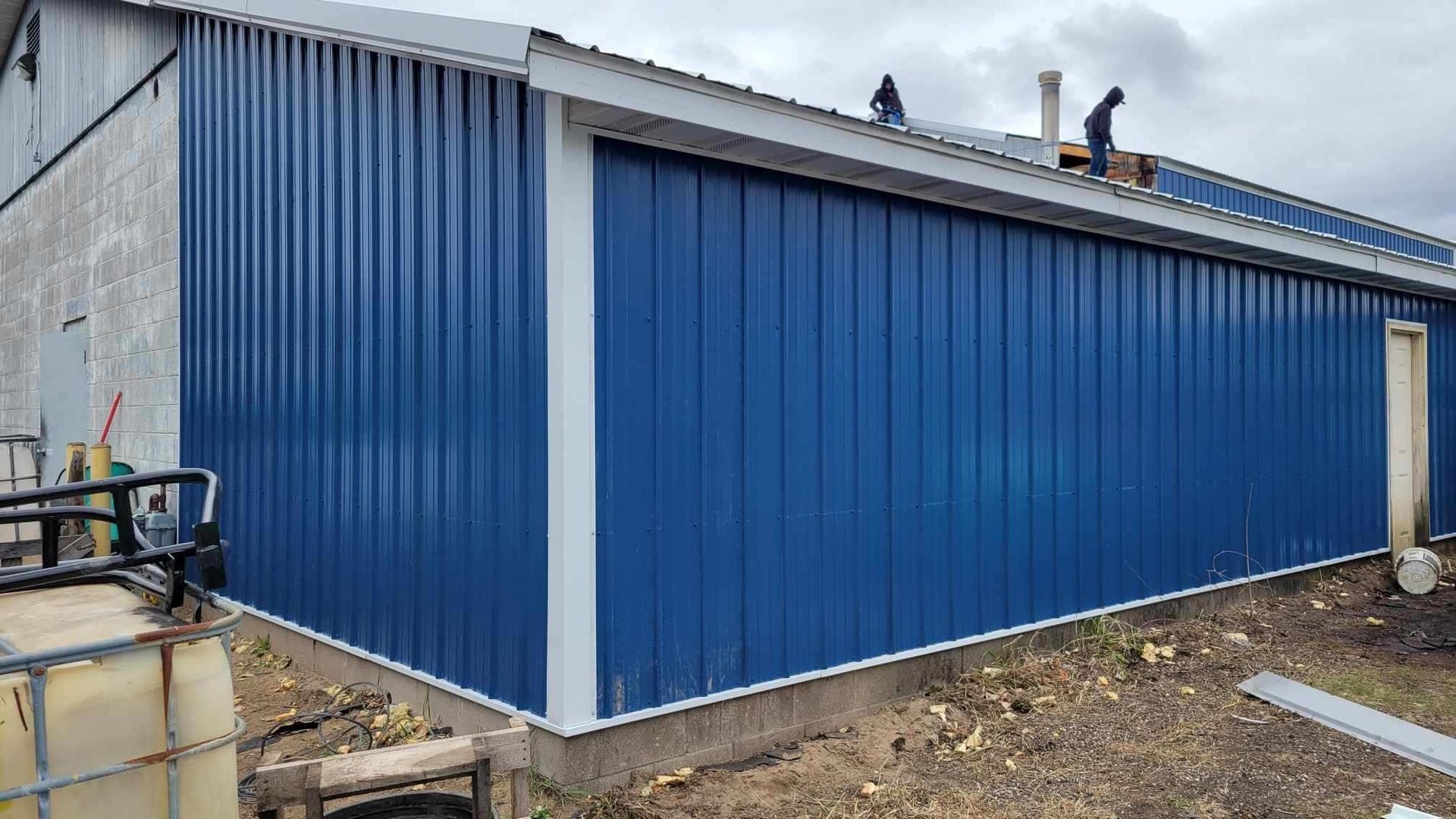 A blue metal building with a white trim is being built.