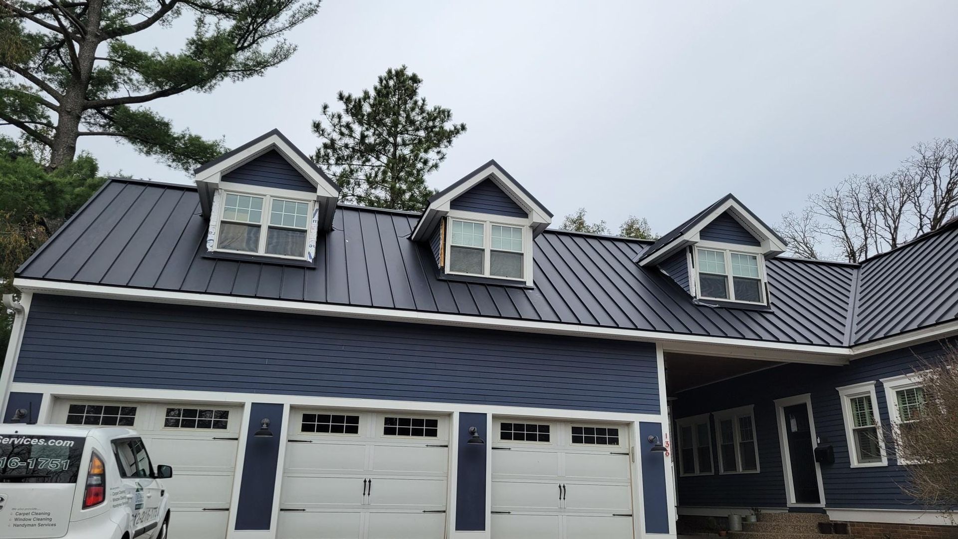 A blue house with a black roof and white garage doors
