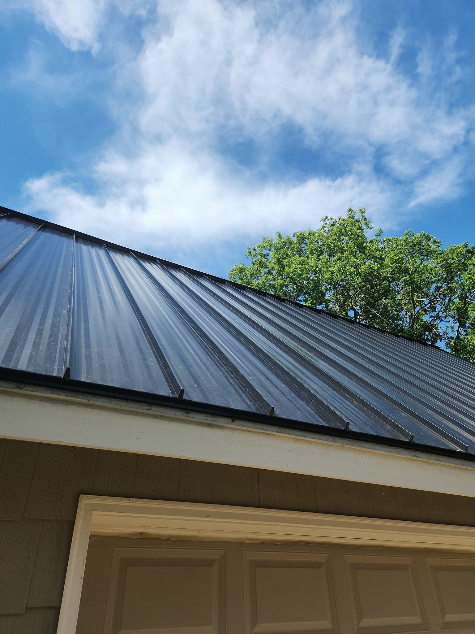 A black metal roof on a house with a blue sky in the background.