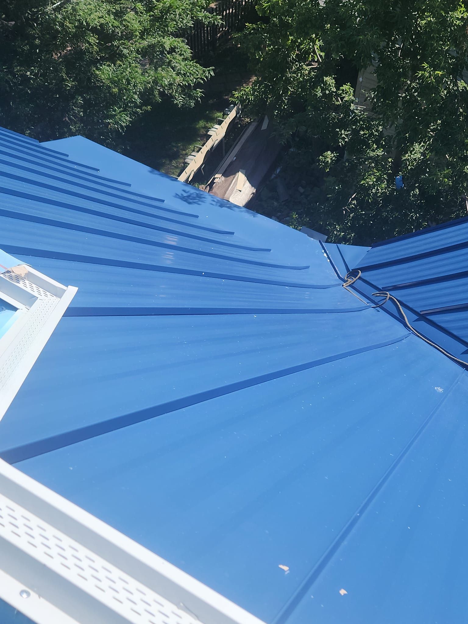 A blue roof with a window and trees in the background.