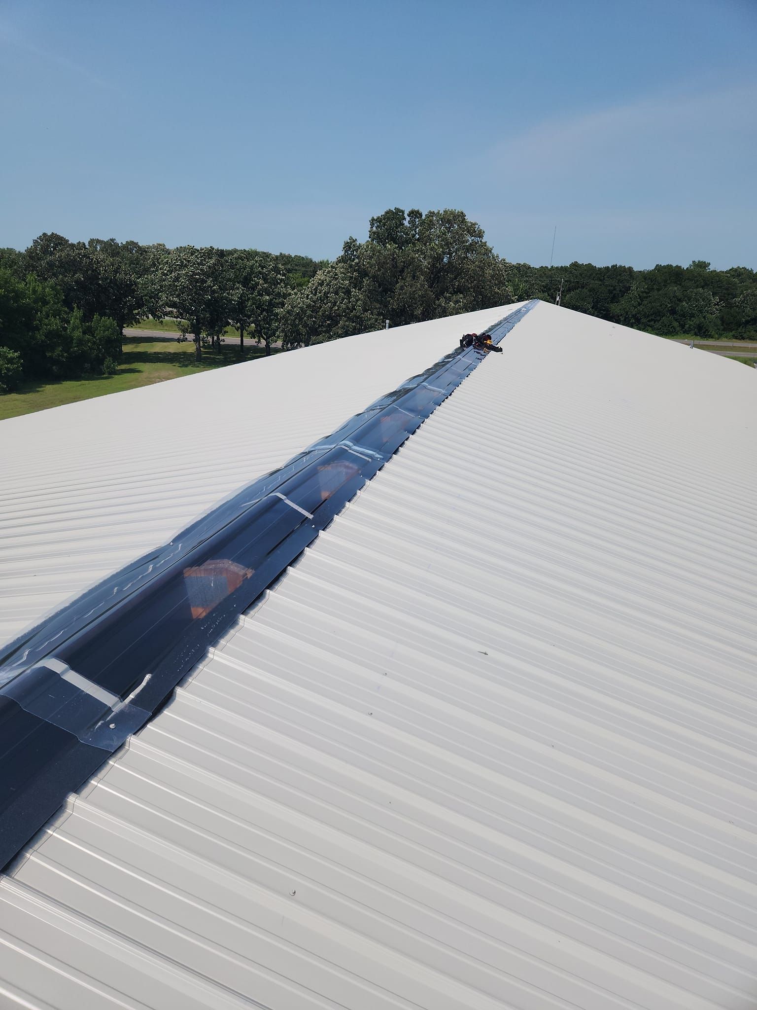 A white roof with a black gutter and trees in the background.