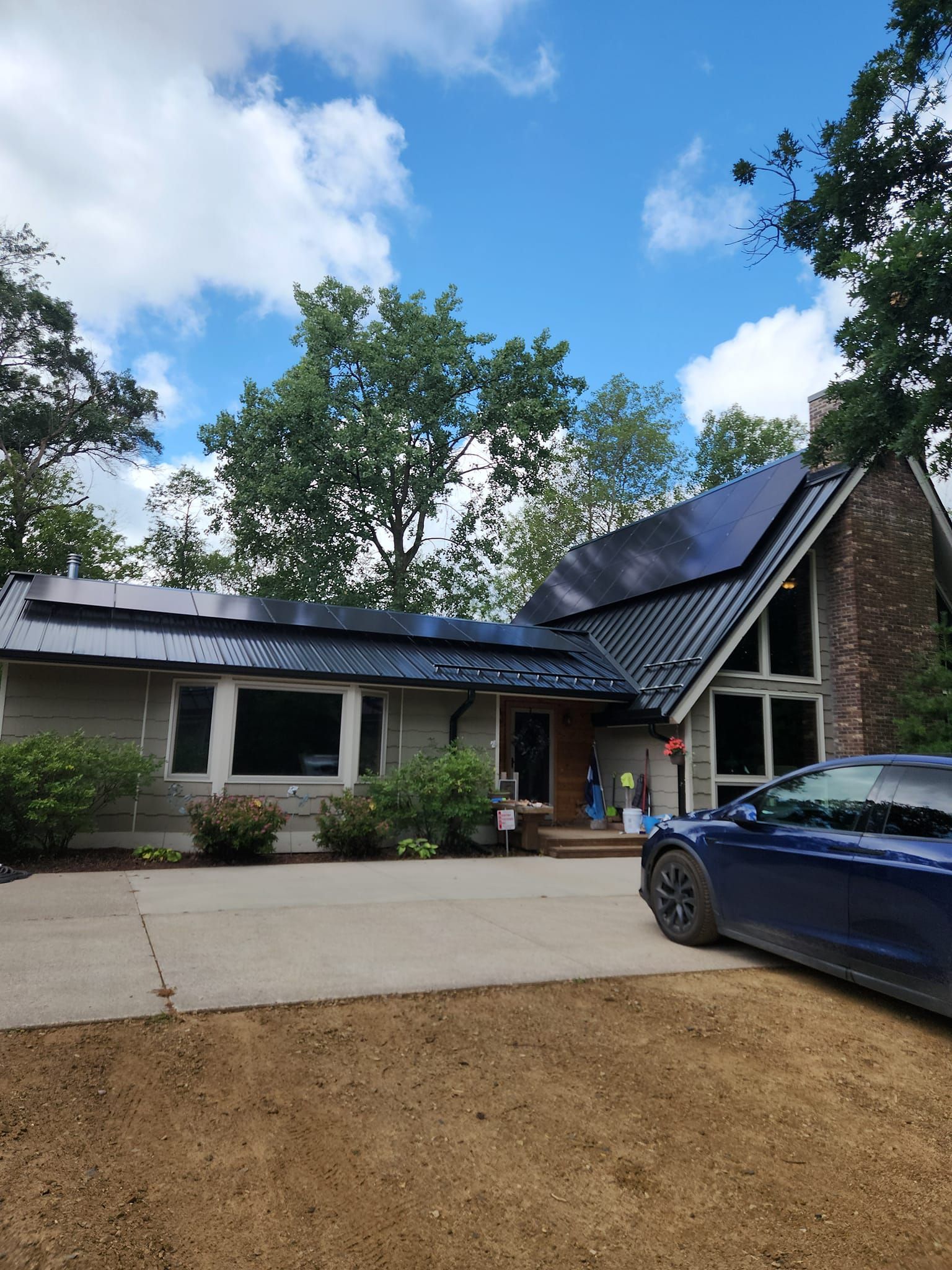 A blue car is parked in front of a house with solar panels on the roof.