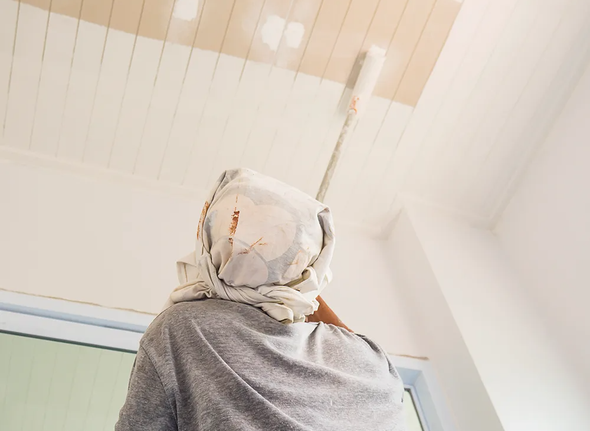 Person in a light gray top and headscarf seen from behind, looking up at a bright ceiling.
