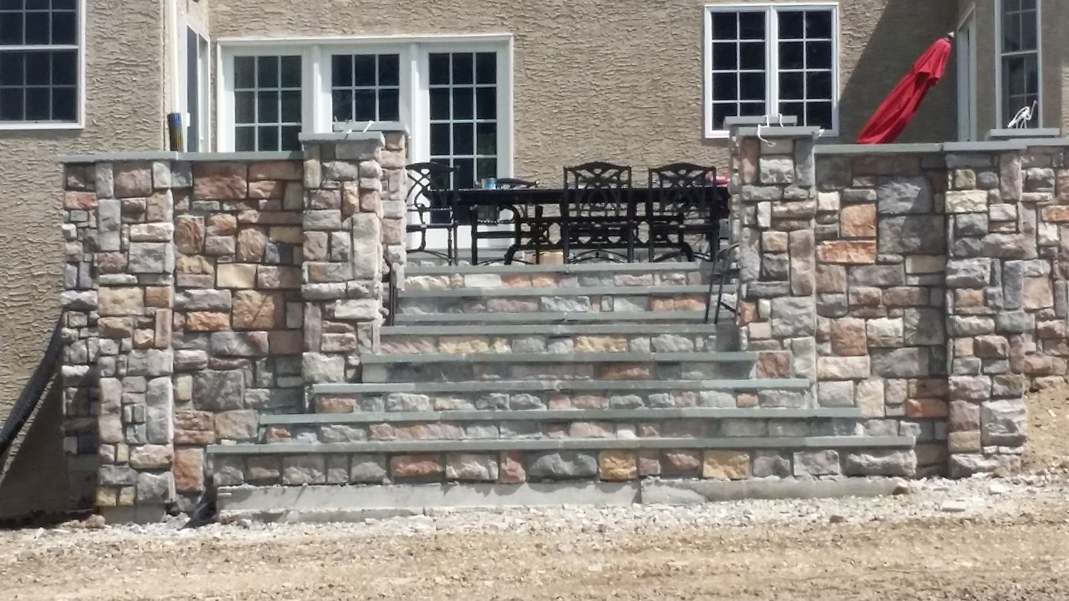 Stone steps leading up to a patio with a table and chairs, flanked by stone walls.