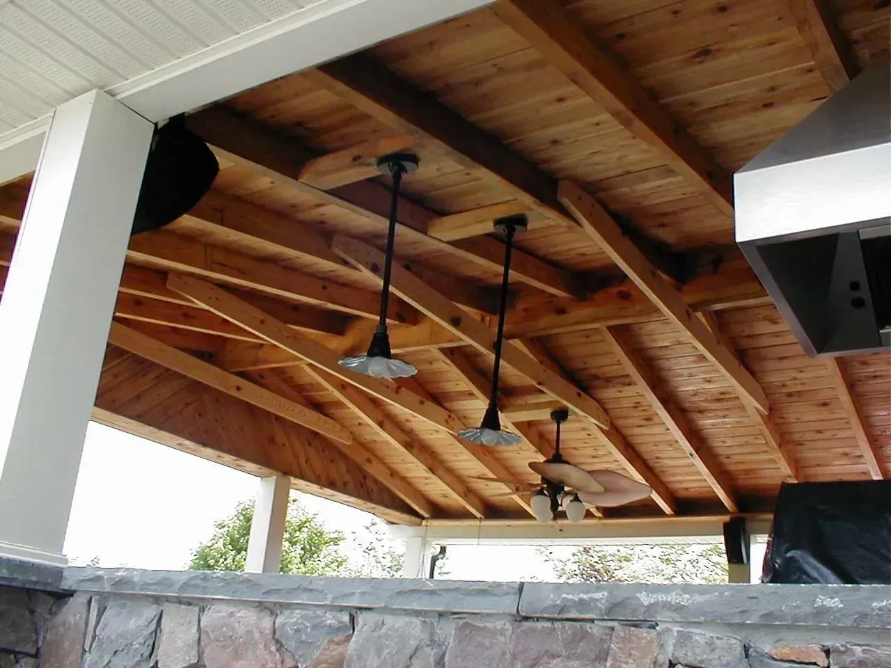Wooden outdoor covered patio with hanging lights, exposed beams, and a stone facade.