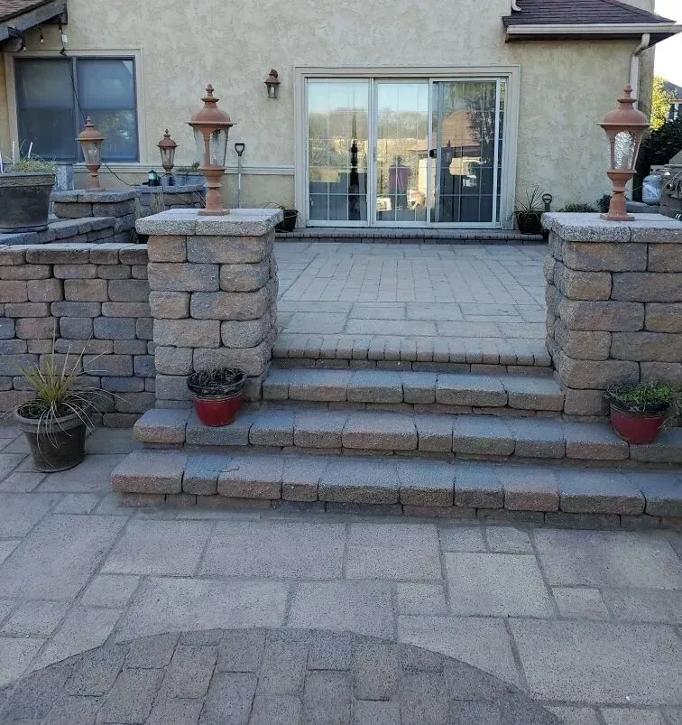 Patio with brick stairs, columns, and lanterns leading to sliding glass doors.