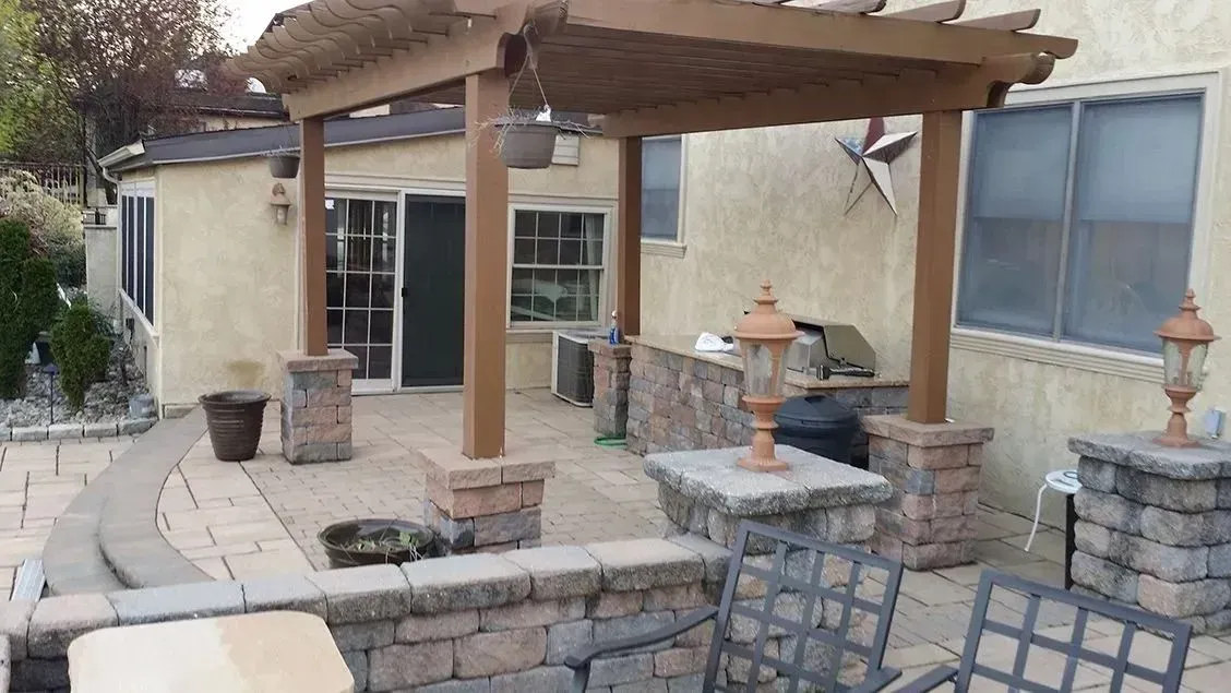 Outdoor patio with pergola, brick columns, grill, and stone pavers.