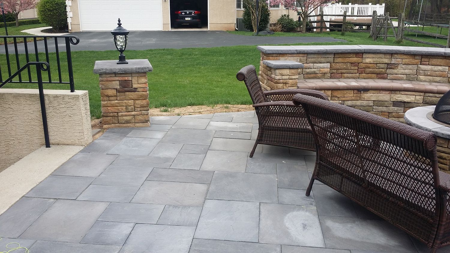 Patio with blue stone pavers, wicker furniture, stone wall with seating, and a decorative pillar.