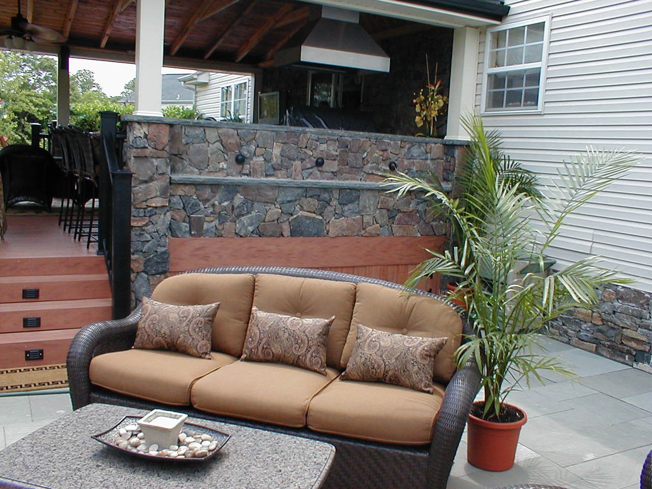 Outdoor patio with a brown wicker sofa, stone wall, and potted plant.