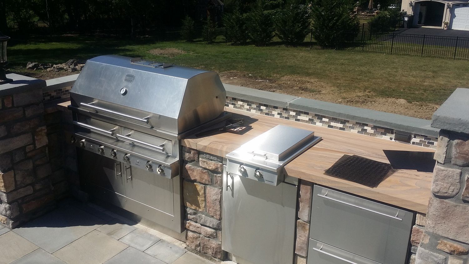 Outdoor stainless steel grill and countertop built into a stone structure on a patio.