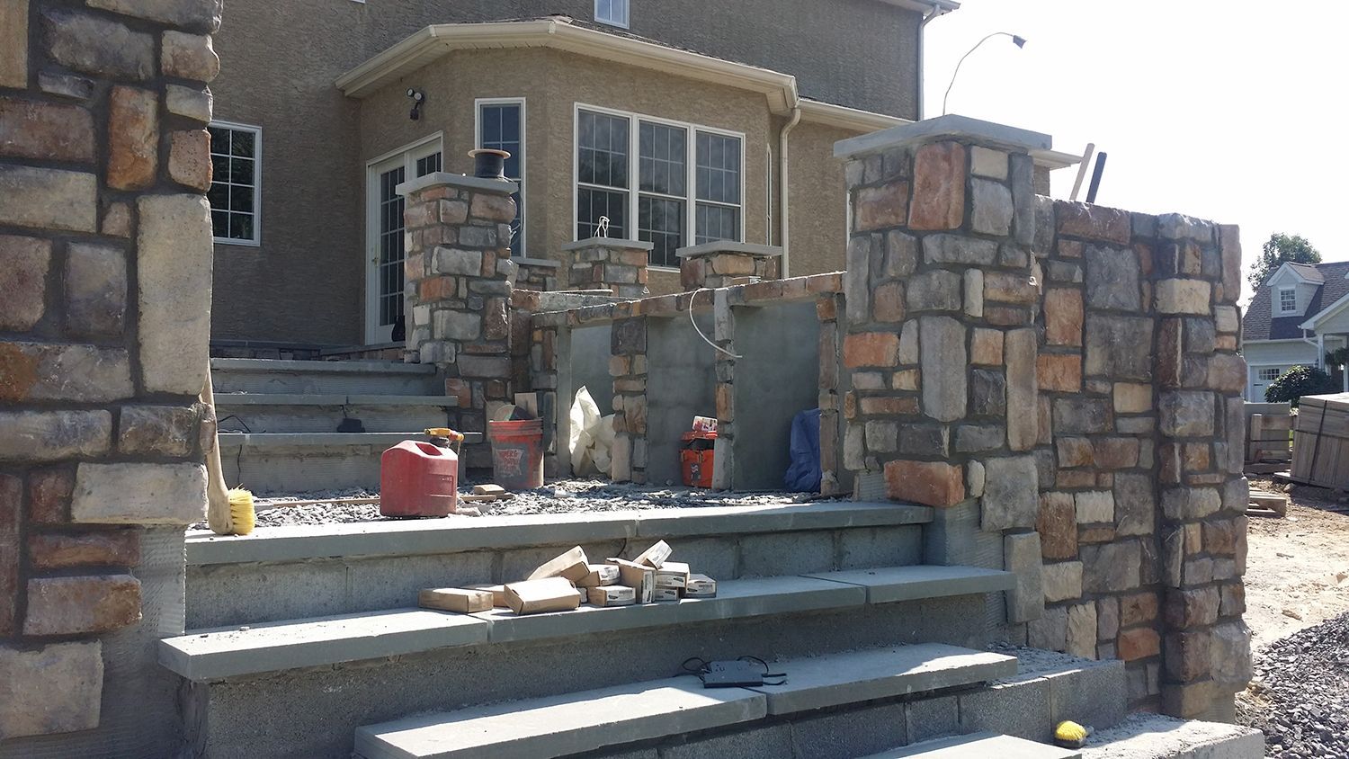 Stone-faced entry stairs of a house under construction; tools, buckets, and materials are present.