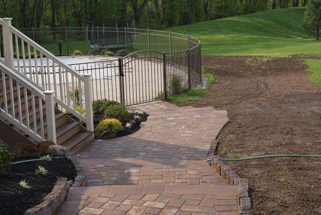 Brick patio with stairs leading to a deck overlooking a yard and pool.