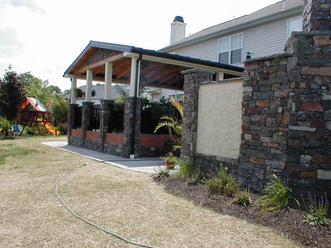 Backyard patio with stone columns, stone wall, and a covered roof.