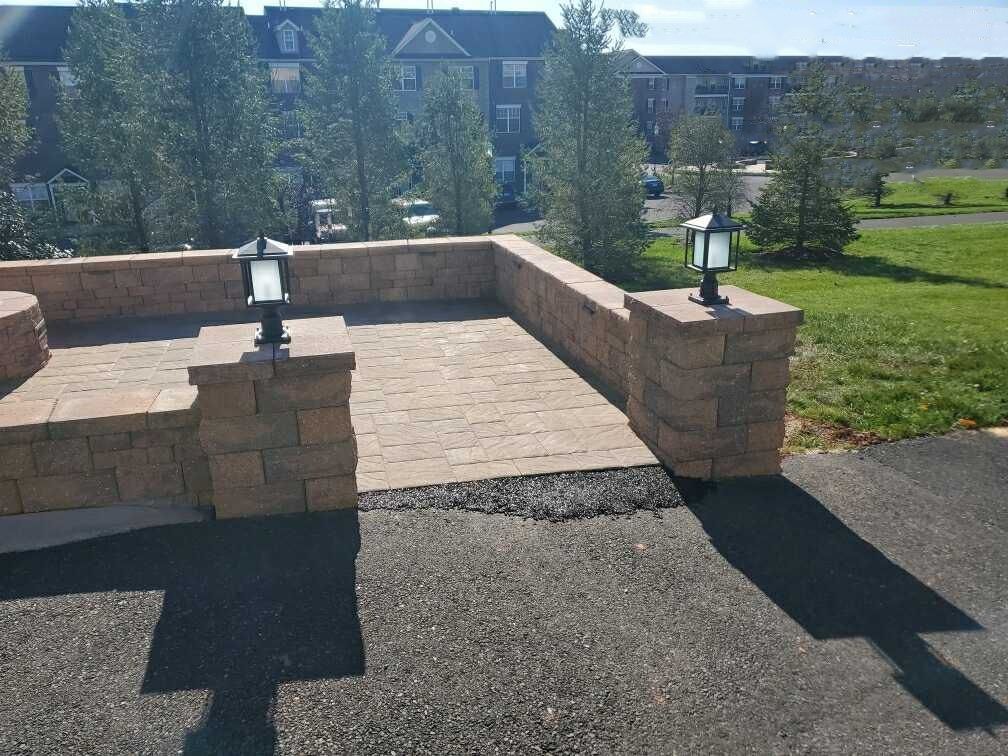 A paved patio with low brick walls, topped with lights, and a grassy area in the background.