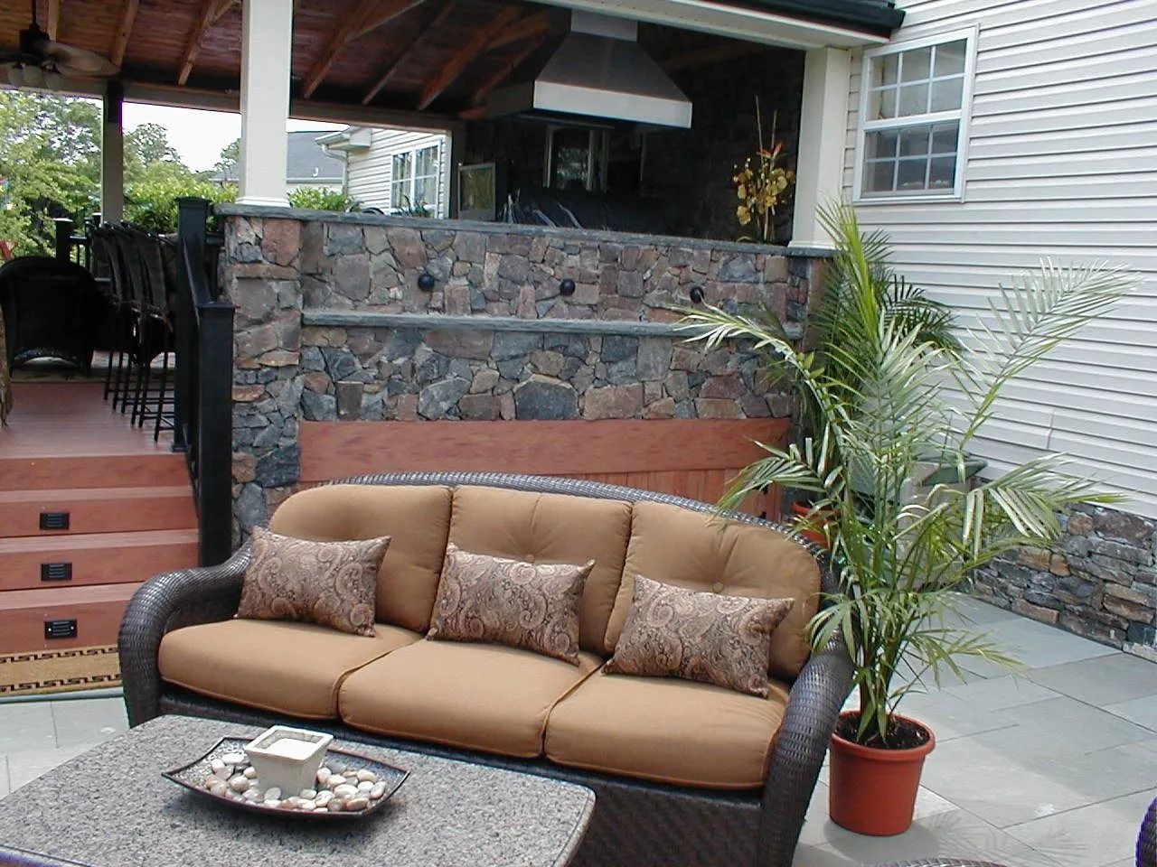 Outdoor seating area with a brown couch, stone wall, and potted plant.