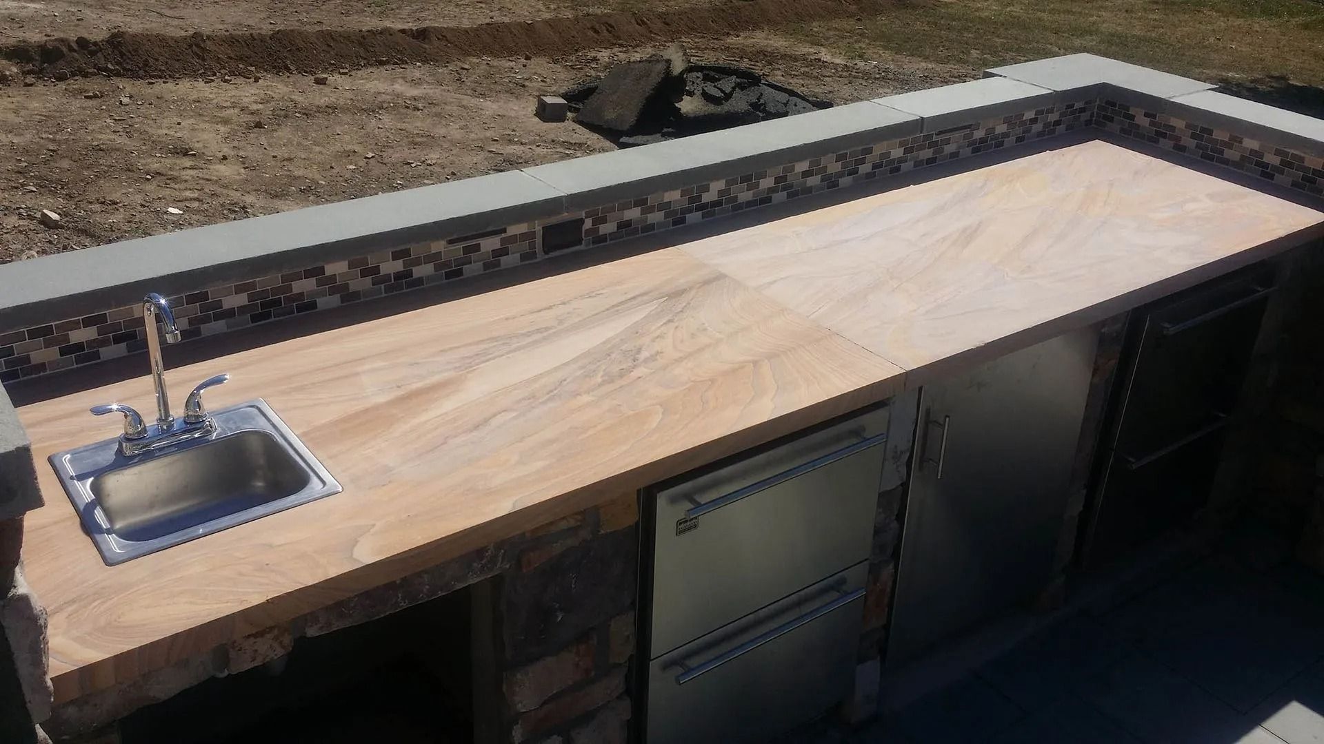Outdoor kitchen with sink, countertop, and stainless steel appliances.