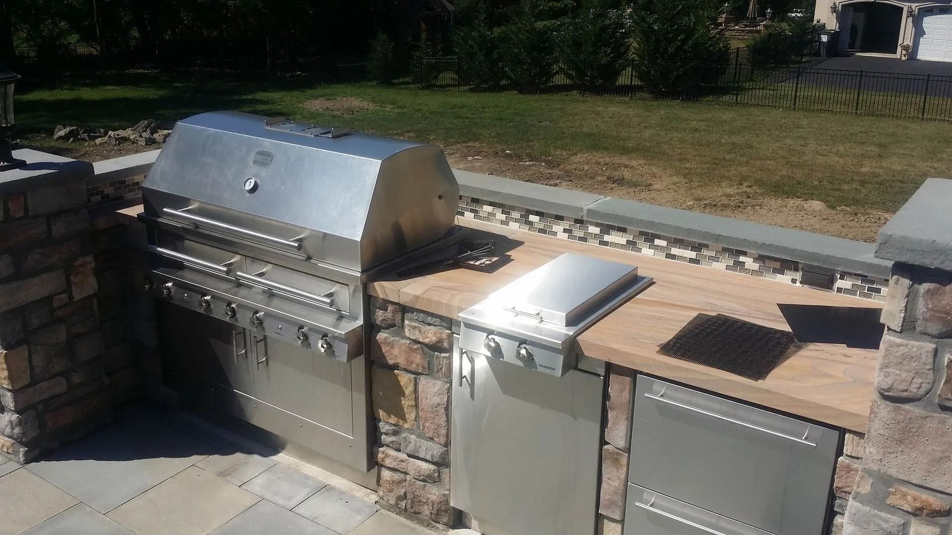 Outdoor kitchen with stainless steel grill, side burner, stone facade, and wooden countertop.