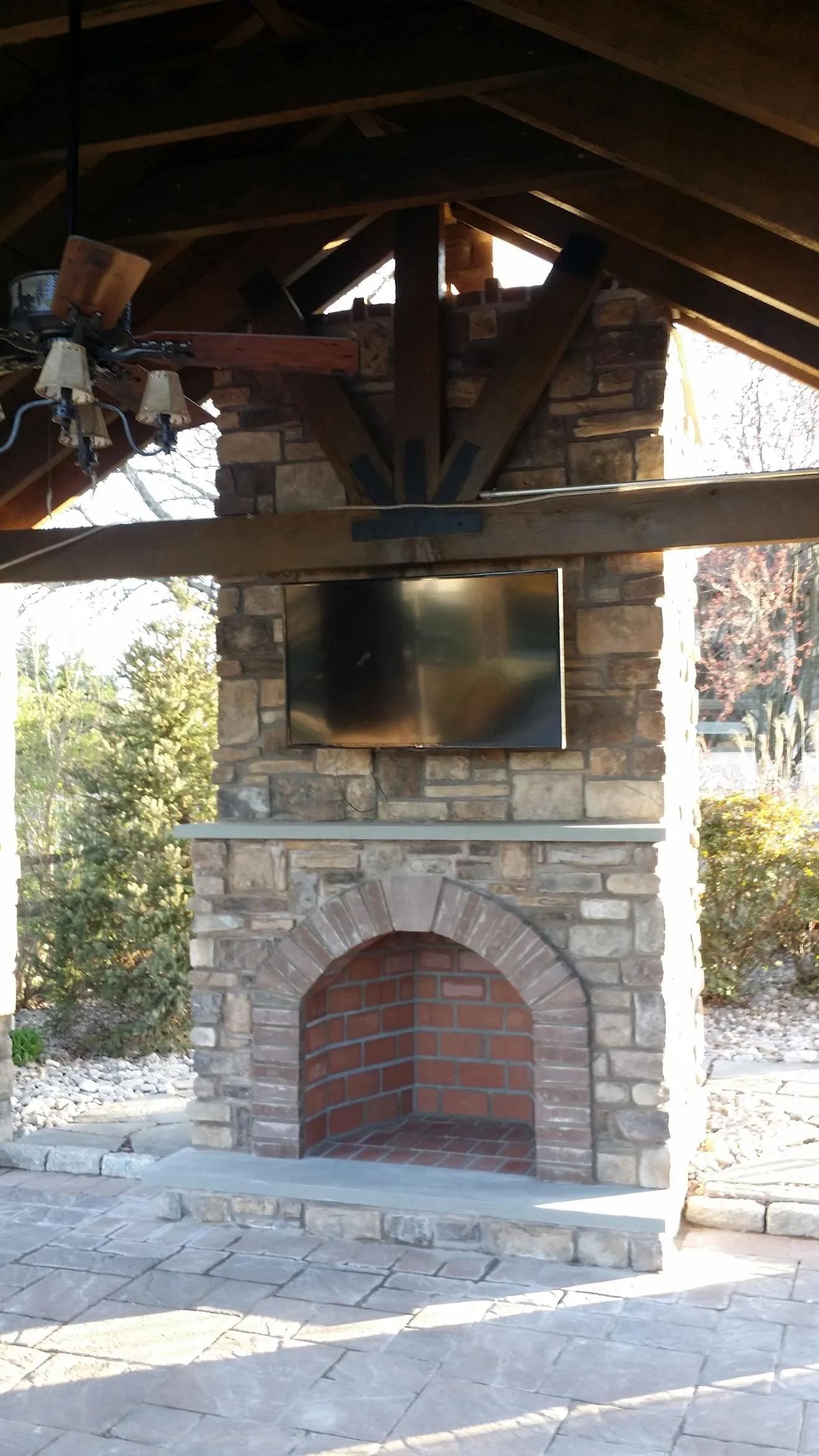 Stone fireplace with brick firebox, beneath a wooden roof and a mounted TV screen.