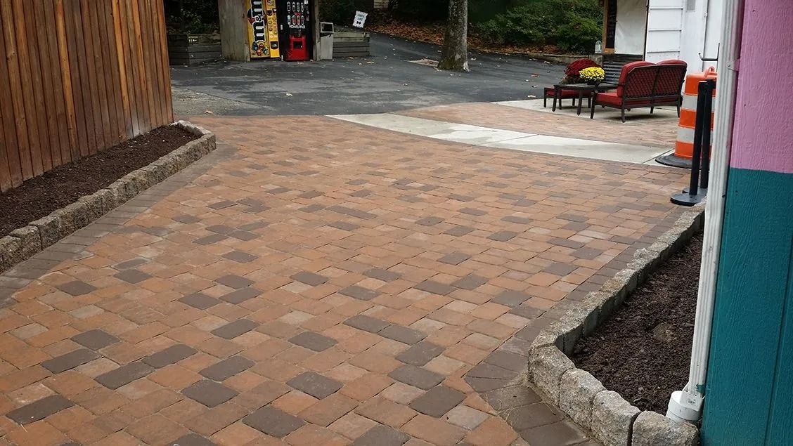 Brick paved patio with brown and reddish bricks, bordered by dark mulch beds, adjacent to a wooden wall.