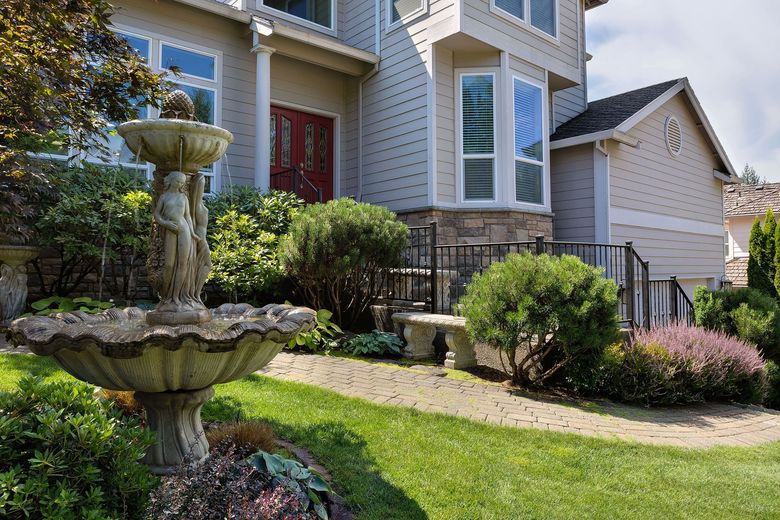 Stone fountain in a well-manicured yard in front of a house.