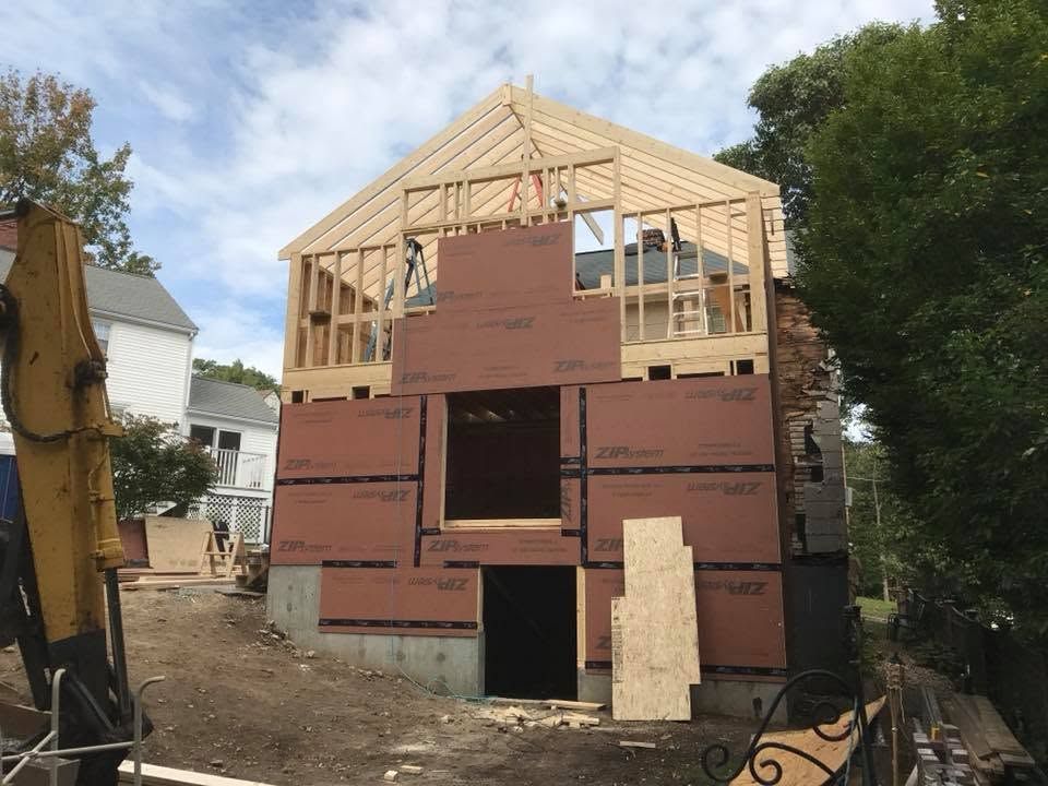 Partially built house with exposed wood framing and red exterior sheathing on a dirt lot