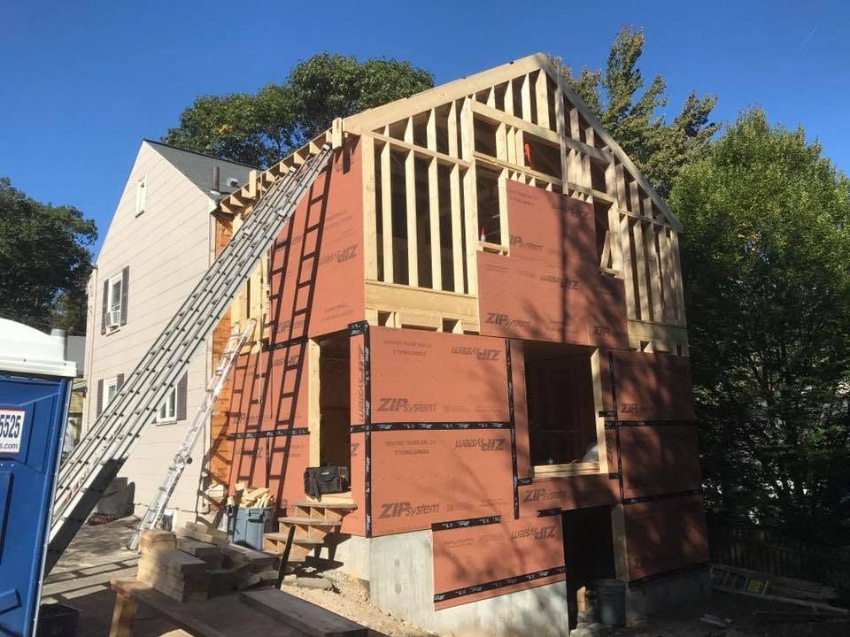 House under construction with ladder, exposed framing, and orange insulation panels in a sunny yard
