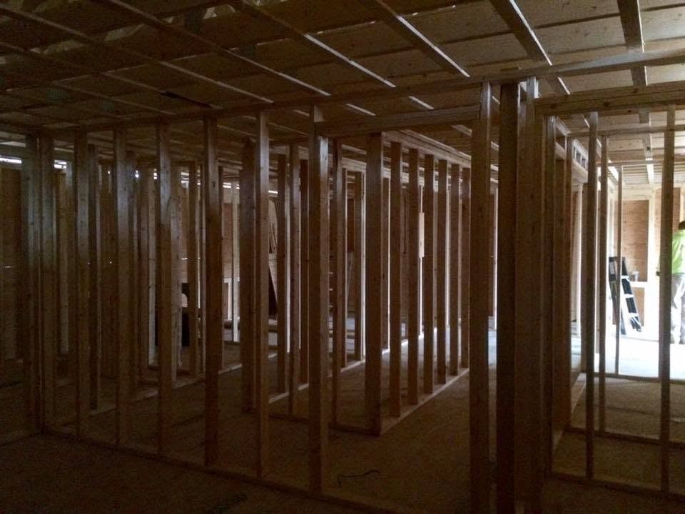 Interior framed with unfinished wooden studs in a construction site, with light coming through an open doorway.