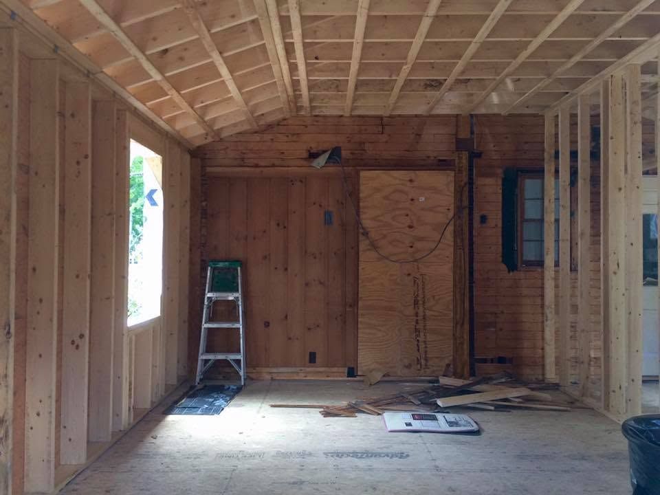 Unfinished wood-framed interior under construction with a ladder near a bright doorway.