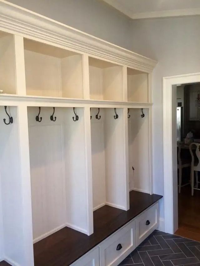 Built-in mudroom bench and cubbies with hooks, white cabinets, and dark wood seat under crown molding