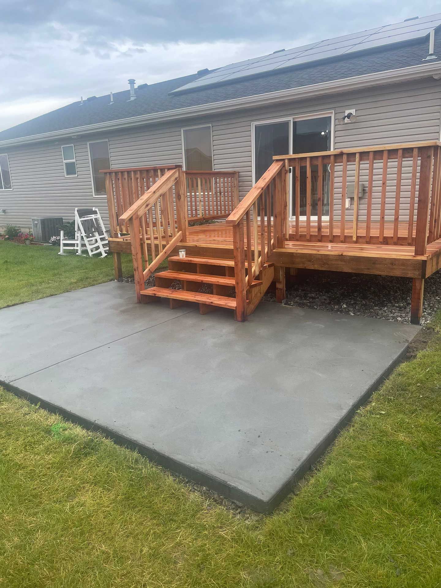 concrete patio with wooden deck and steps, next to a grassy lawn