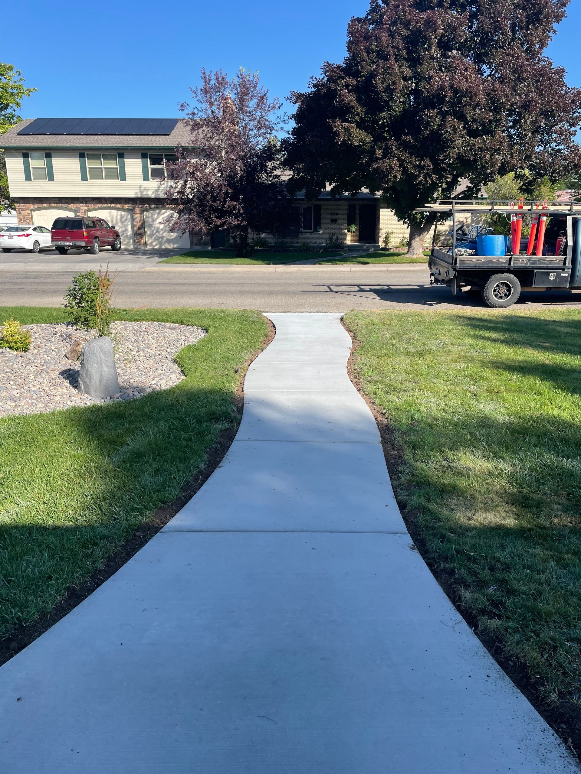 Concrete sidewalk curves through green lawn towards residential street with a truck.