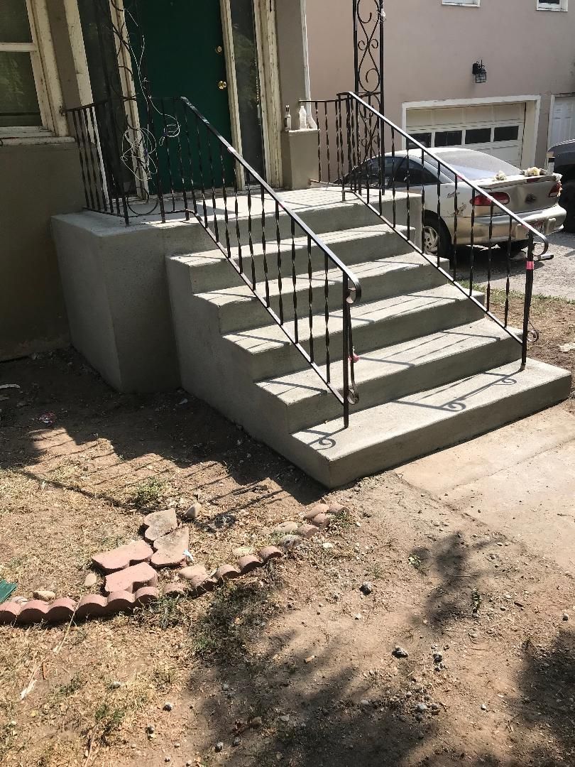 A set of concrete stairs with a metal railing in front of a house.