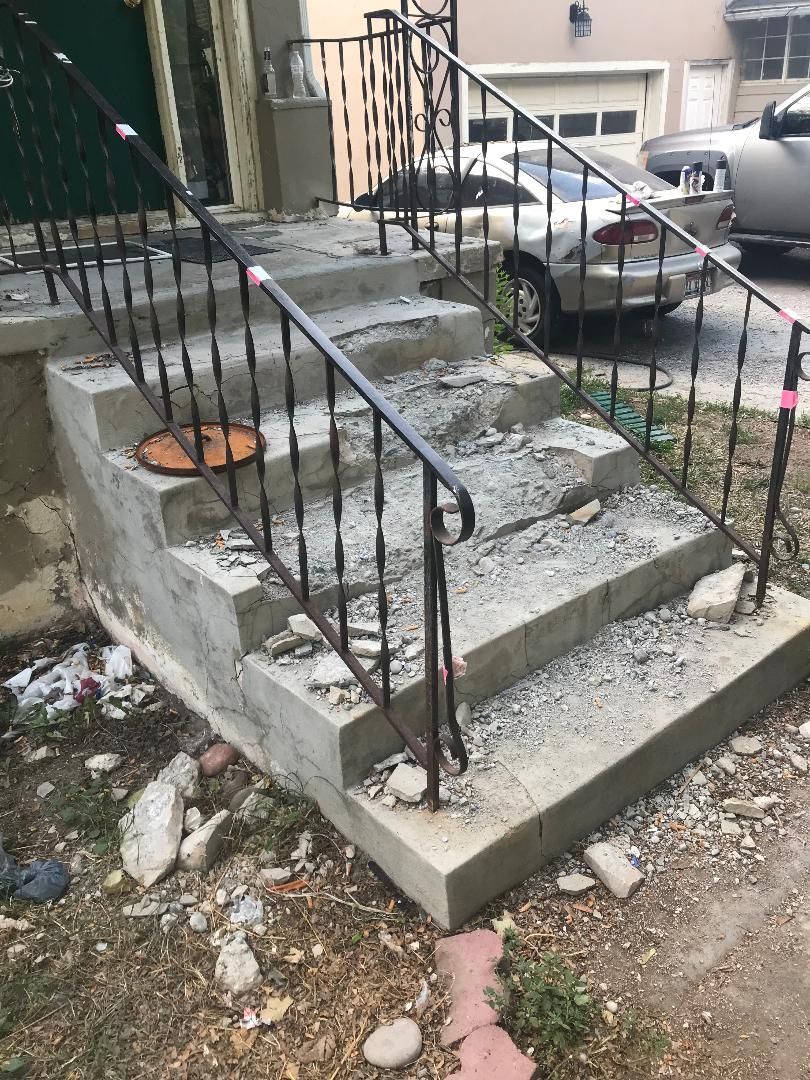 A set of stairs with a wrought iron railing and a car parked in the background.