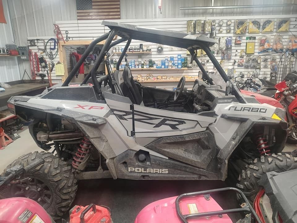 Gray Polaris RZR Turbo parked indoors with tools and a US flag in the background.