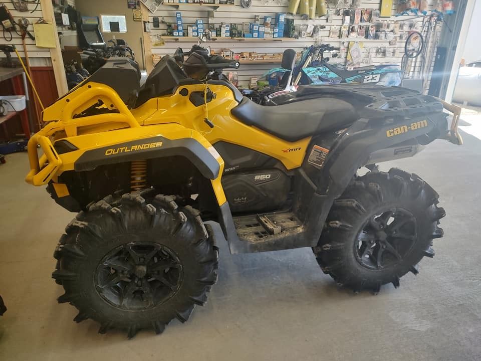 Yellow and black Can-Am Outlander ATV with large mud tires, parked indoors, viewed from the side.