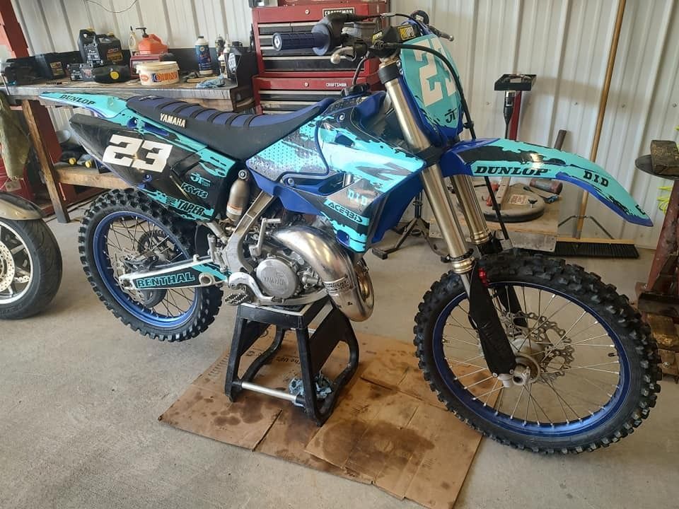 Blue and black motocross motorcycle on a stand, indoors. Number 23 on it.