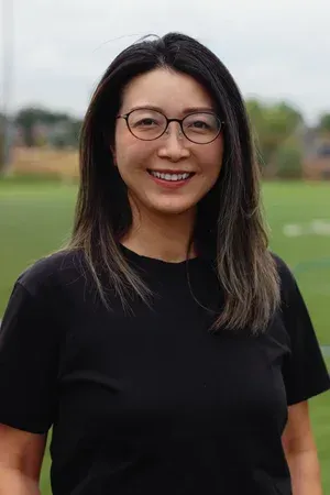 Smiling woman with glasses in a black shirt standing outdoors on a grassy field