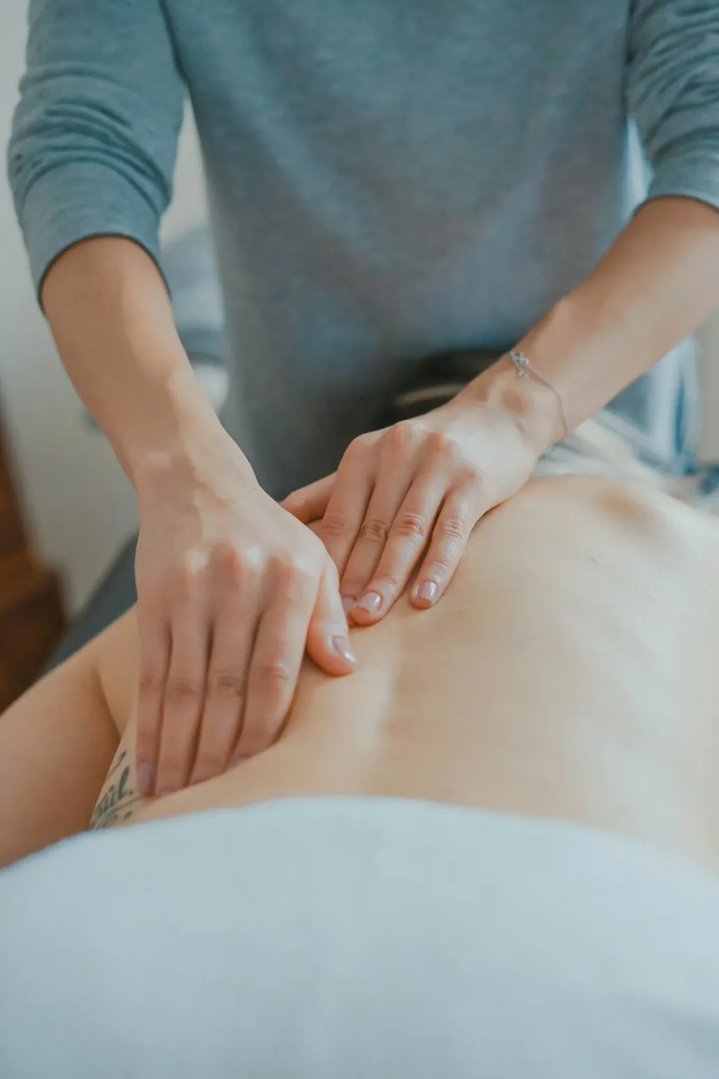 Hands performing a massage on a person's bare back in a softly lit room.