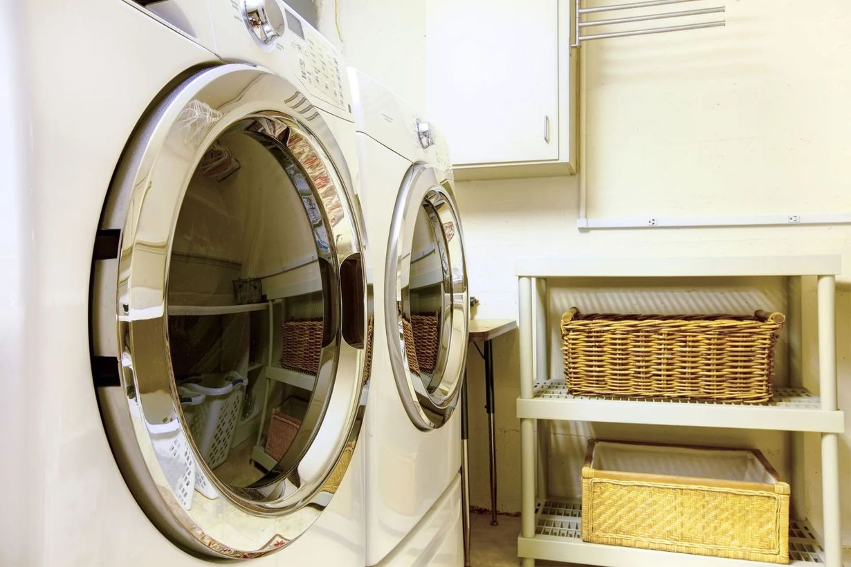 White washer and dryer in a laundry room; shelves with baskets sit beside them.
